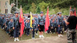 Des élèves en uniforme de l’Armée populaire, portant des sacs à dos sur lesquels sont imprimés le portrait du président Mao et le slogan « Servir le peuple ».